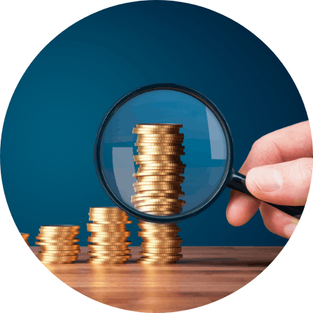 Stacked gold coins on a table being looked at with a magnifying glass