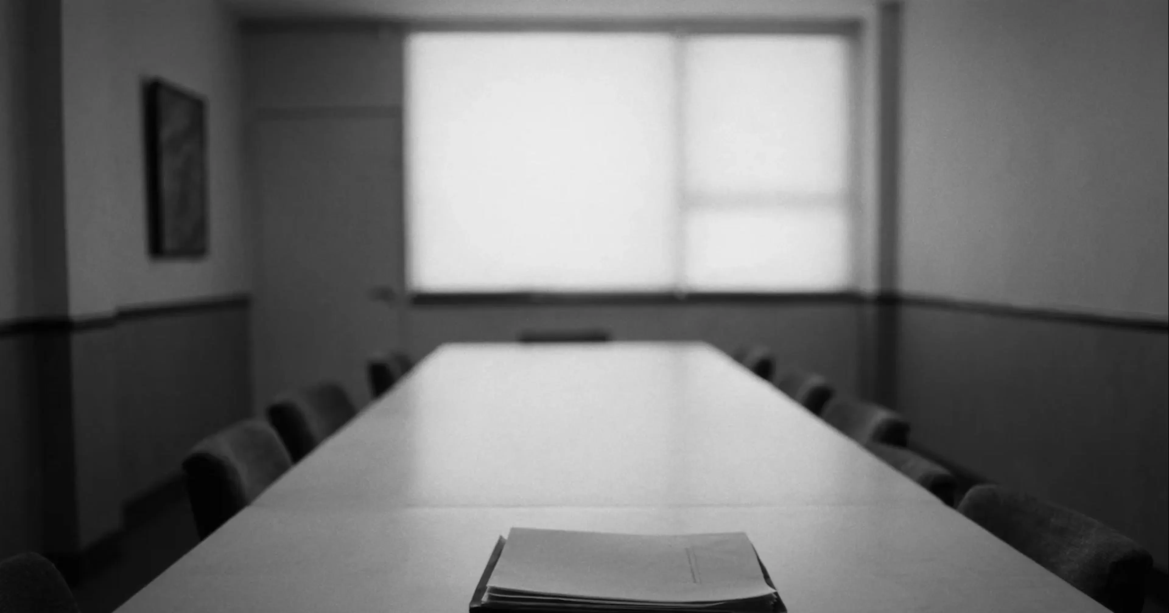 An empty consulting-room table with a single closed folder, the price of outside advice, contemplative black and white