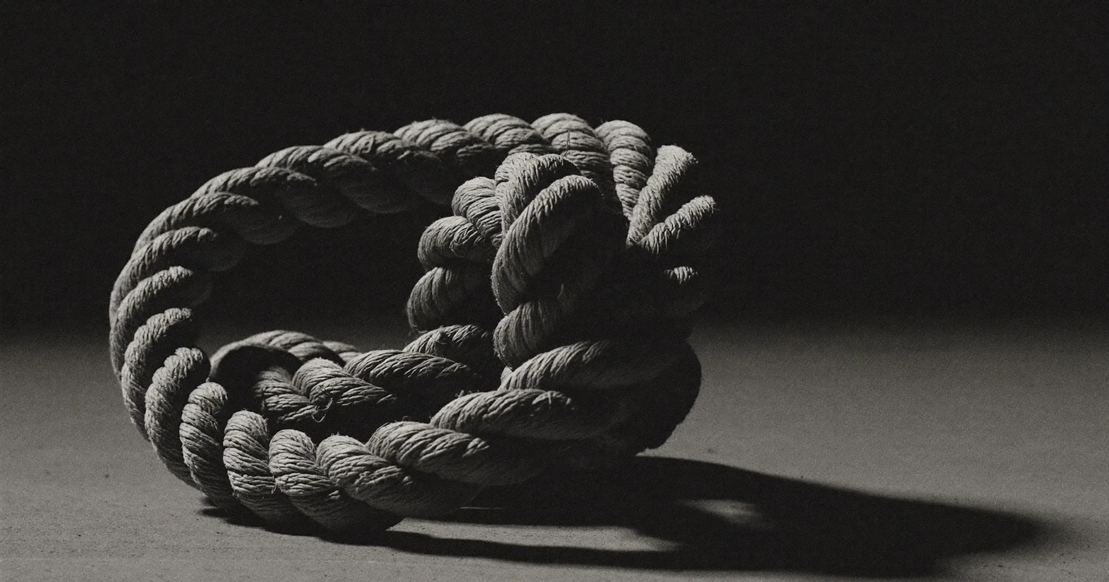A single tangled knot of thick rope, an overwhelmed SME owner facing tangled priorities, contemplative black and white