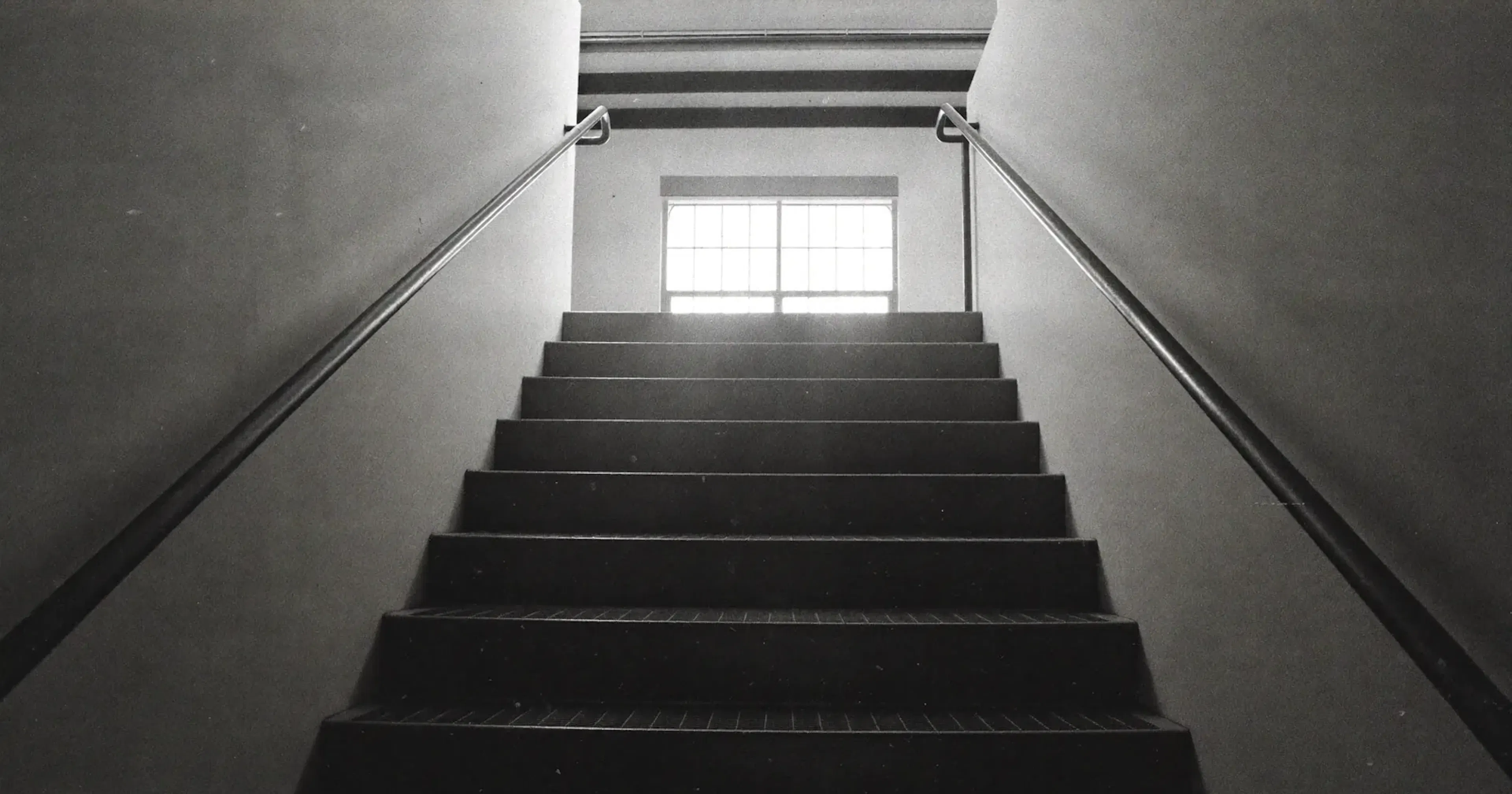 Ascending industrial staircase rising toward light, SME management consulting, the next level, contemplative black and white