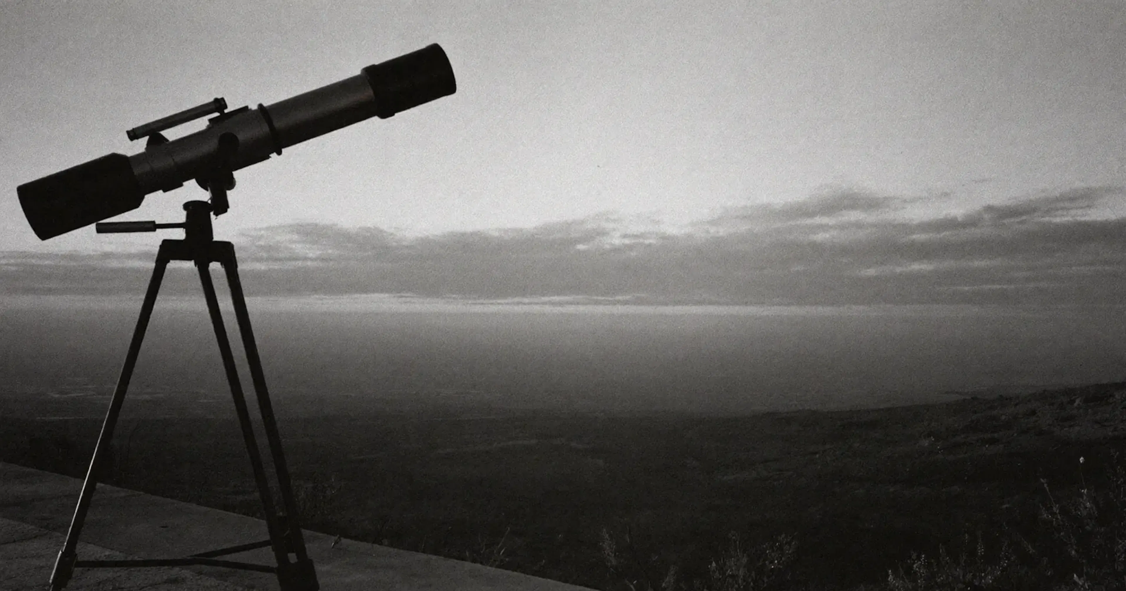 Telescope on a tripod overlooking a valley toward the horizon at dusk, strategic monitoring, foresight, contemplative black and white