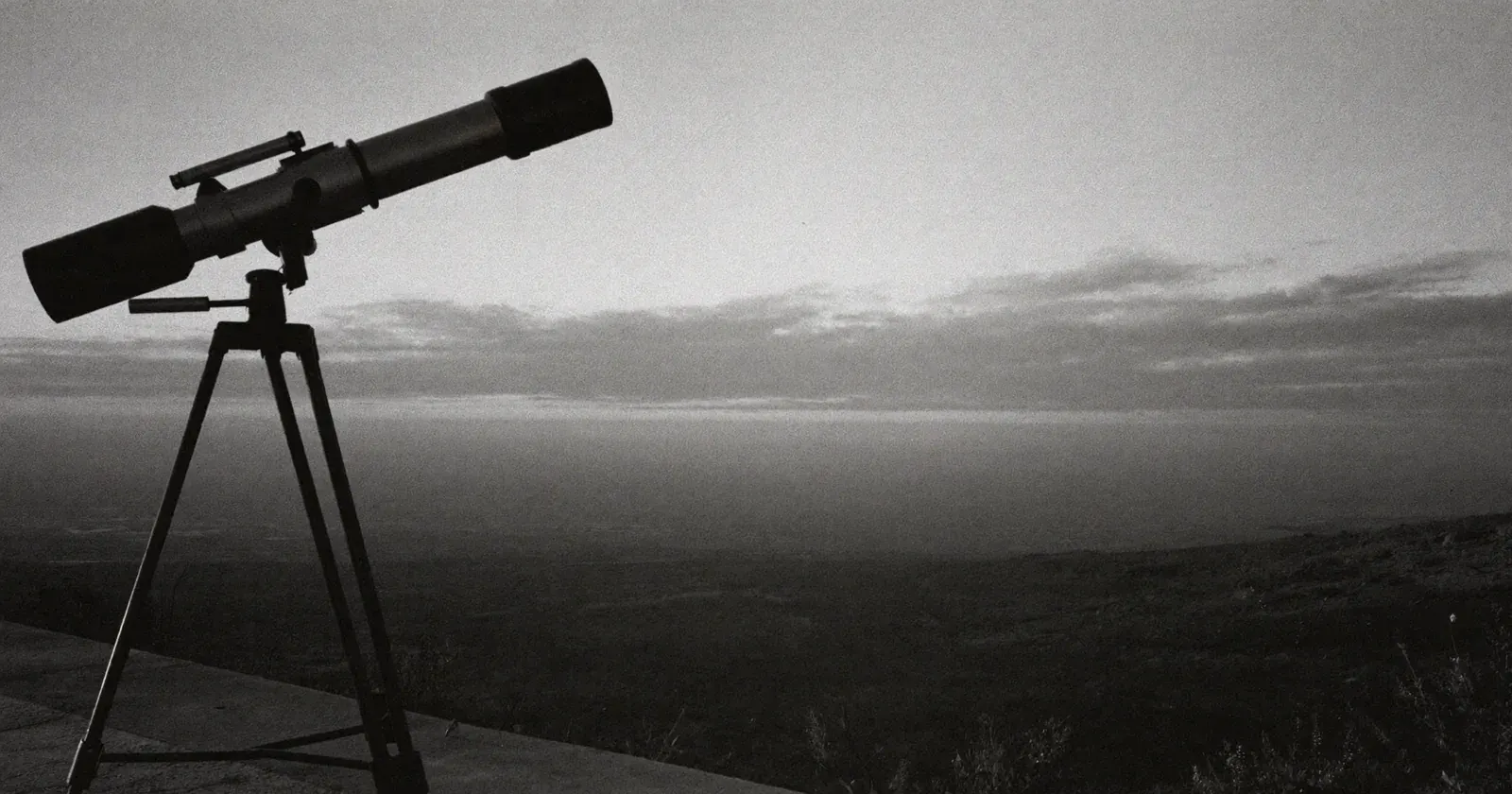 Telescope on a tripod overlooking a valley toward the horizon at dusk, strategic monitoring, foresight, contemplative black and white