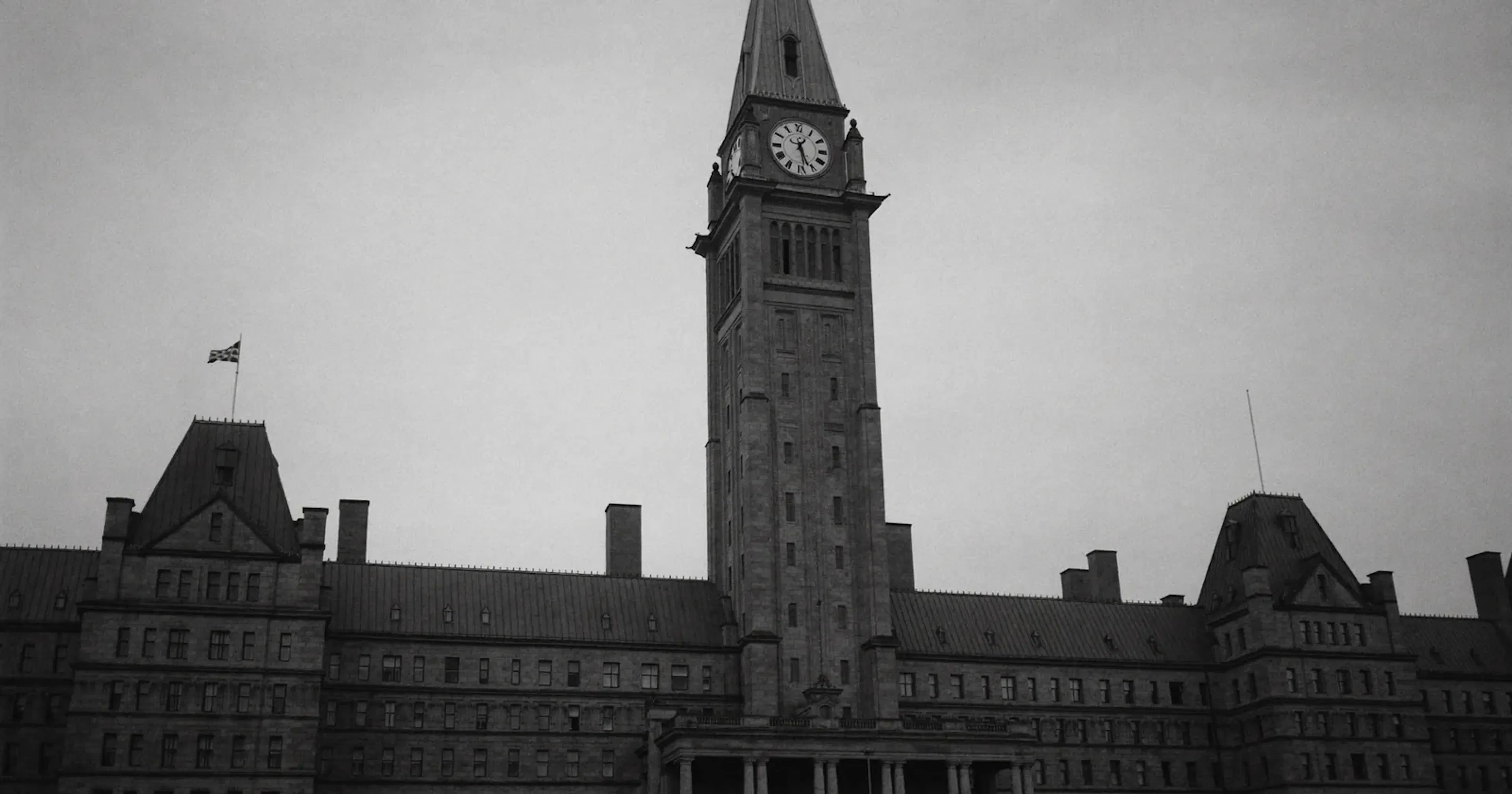 Stately Canadian government building with a neo-gothic clock tower under an overcast sky, Canada's national AI strategy, contemplative black and white