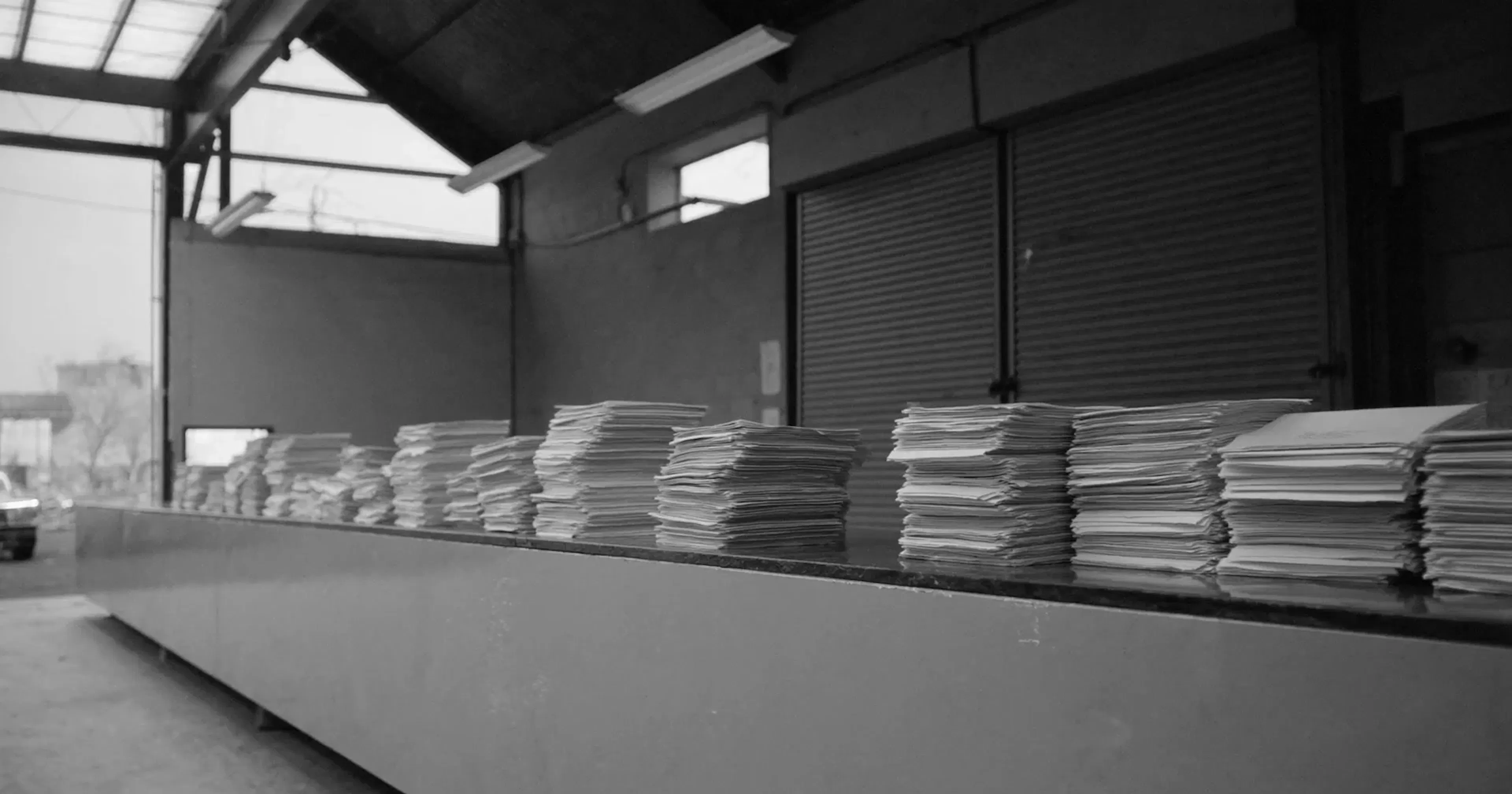 A customs inspection bay with stacked entry paperwork, tariff refund claims, contemplative black and white