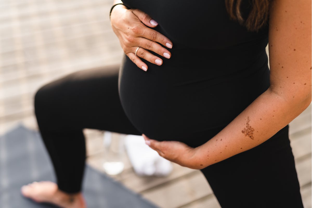 Ausschnitt des Bauches und der Beine einer schwangeren Frau in Yoga-Position.