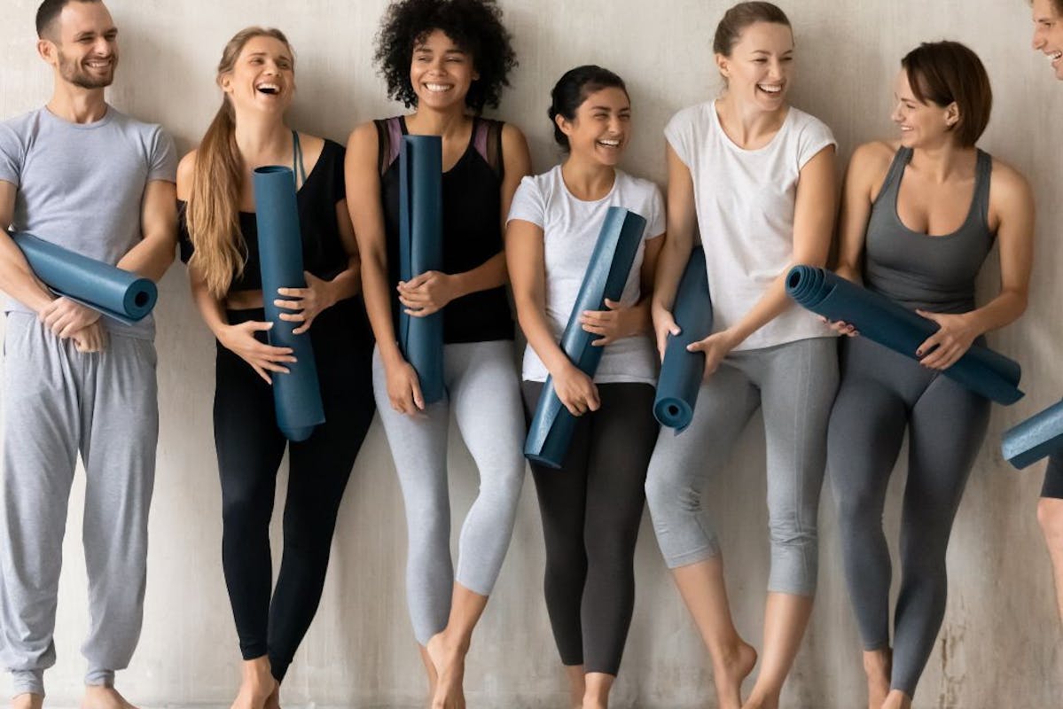 Yogis mit Matten lächelnd nebeneinander an einer Wand