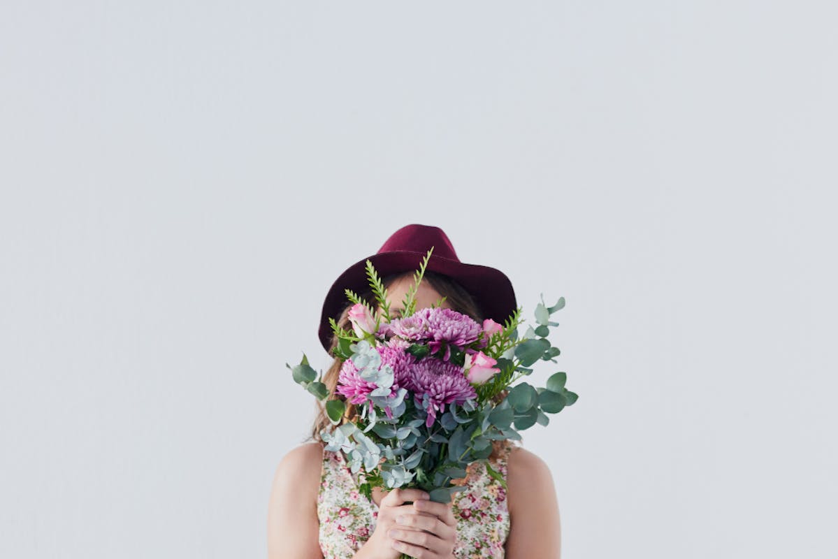 Frau mit Hut hält einen Frühlingsbunten Blumenstrauß vor ihr Gesicht.