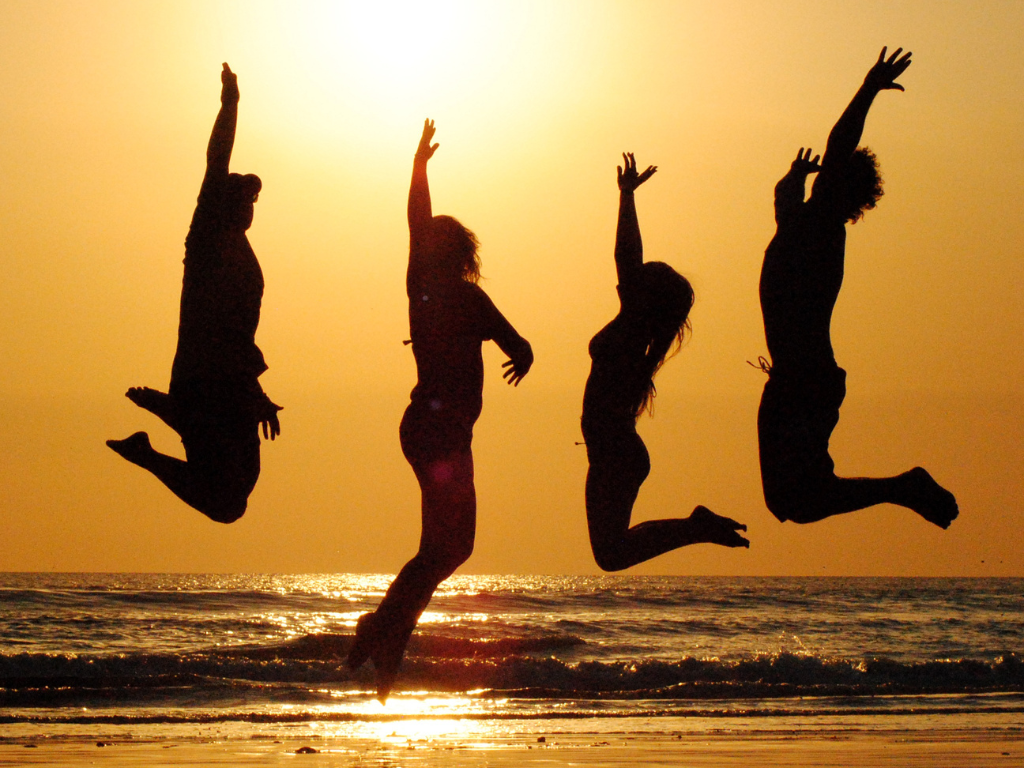 4 Frauen springen am Strand im Sonnenuntergang in die Luft 