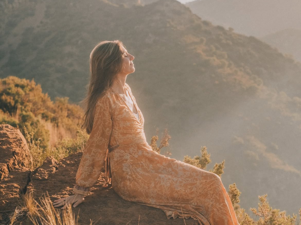 Jeska in Erdfarbenem, fließenden Kleid in der Natur bei Sonnenlicht. 