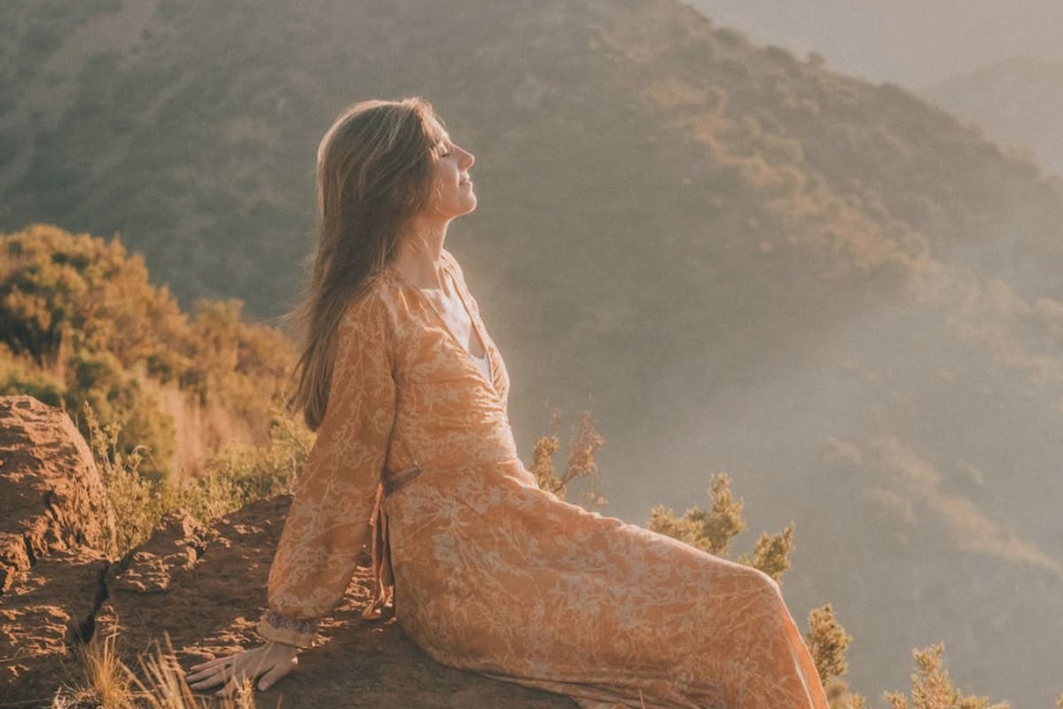 Jeska in Erdfarbenem, fließenden Kleid in der Natur bei Sonnenlicht.