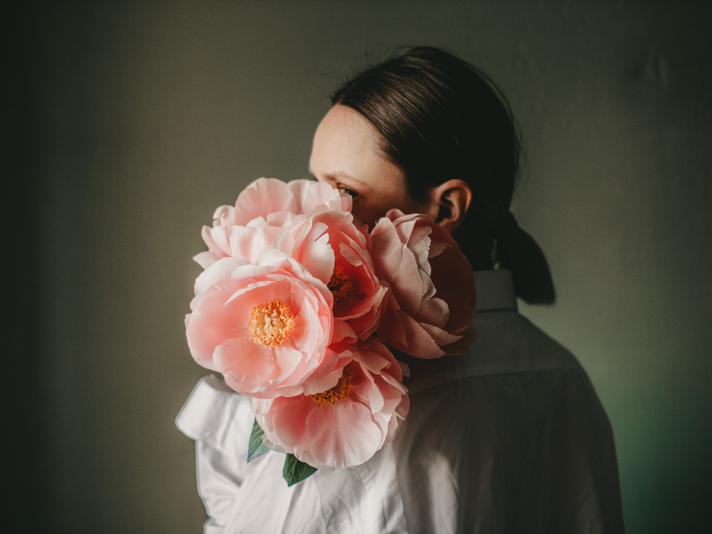 Frau, die riesige Blüten in apricot-farben im Arm hält und ihr Gesicht hinein schmiegt.