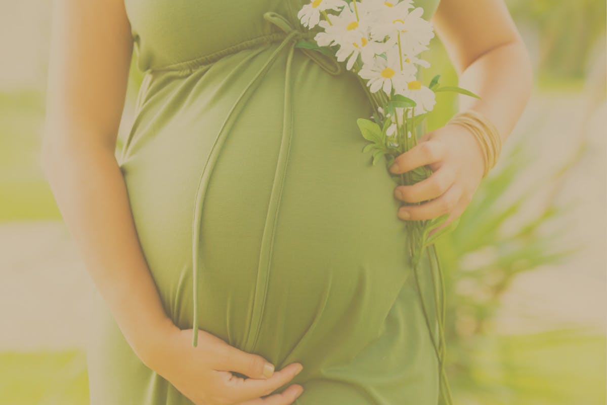 Schwangerer Babybauch bei sommerlichen Farben in hellem grün mit Blumen