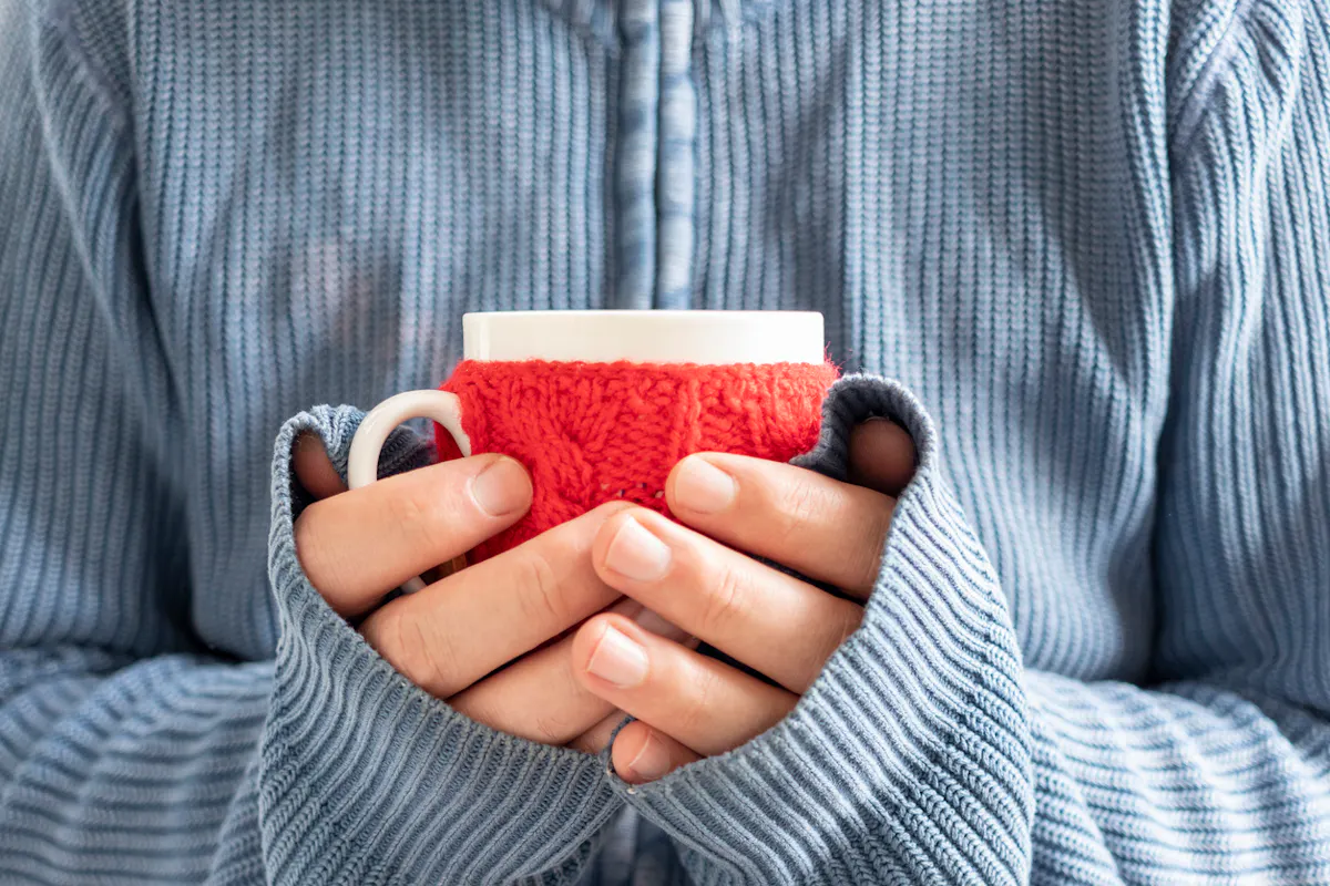 Hände Frau halten Tasse mit Strick eingehüllt.