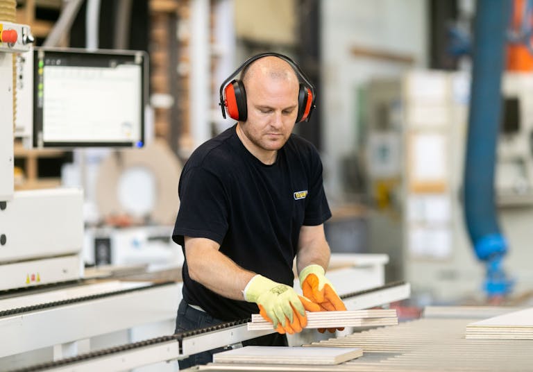 Mivan employee lifting wood from conveyor belt