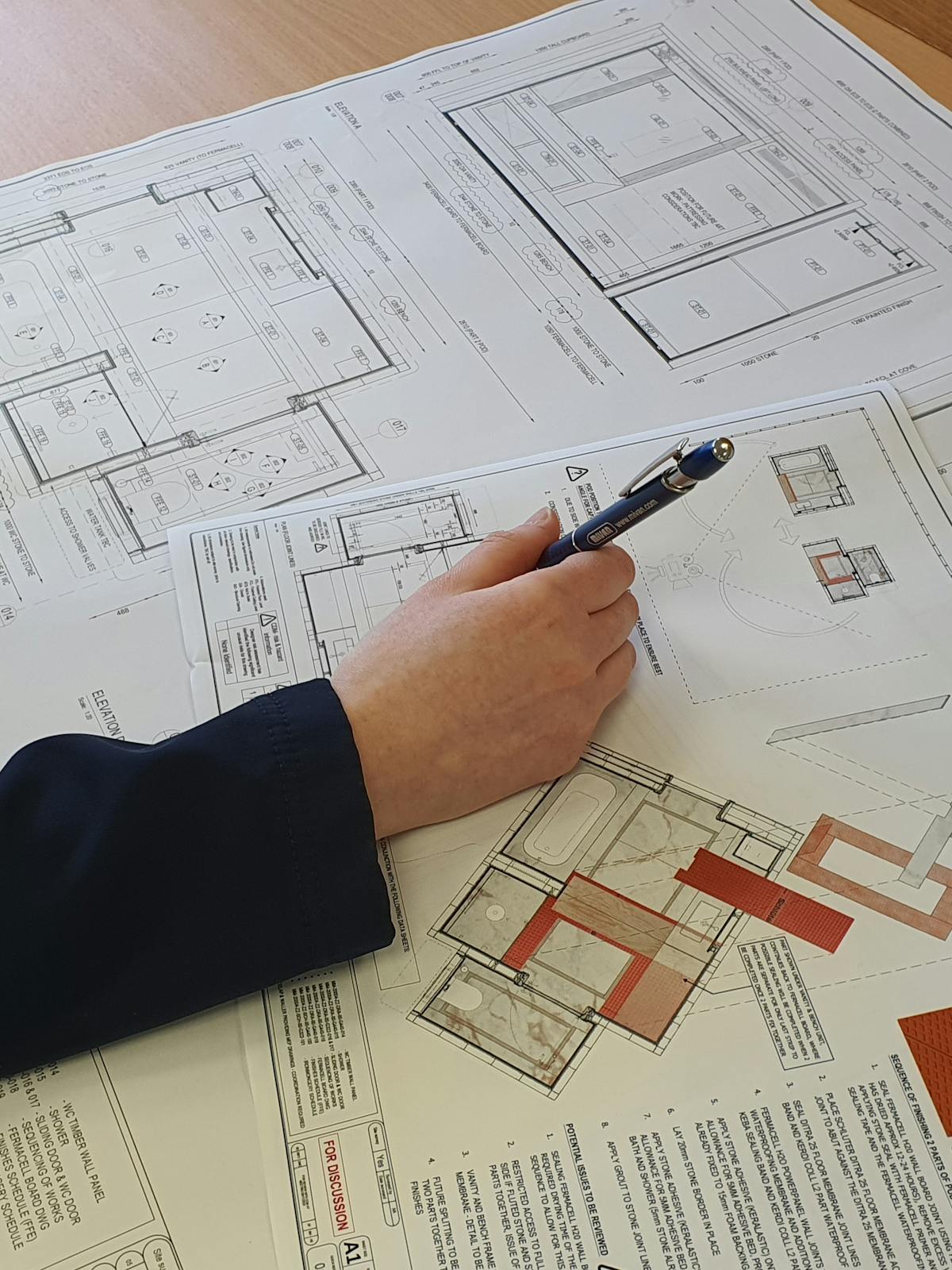 Drawings set on a table with a pen in hand reviewing the content.