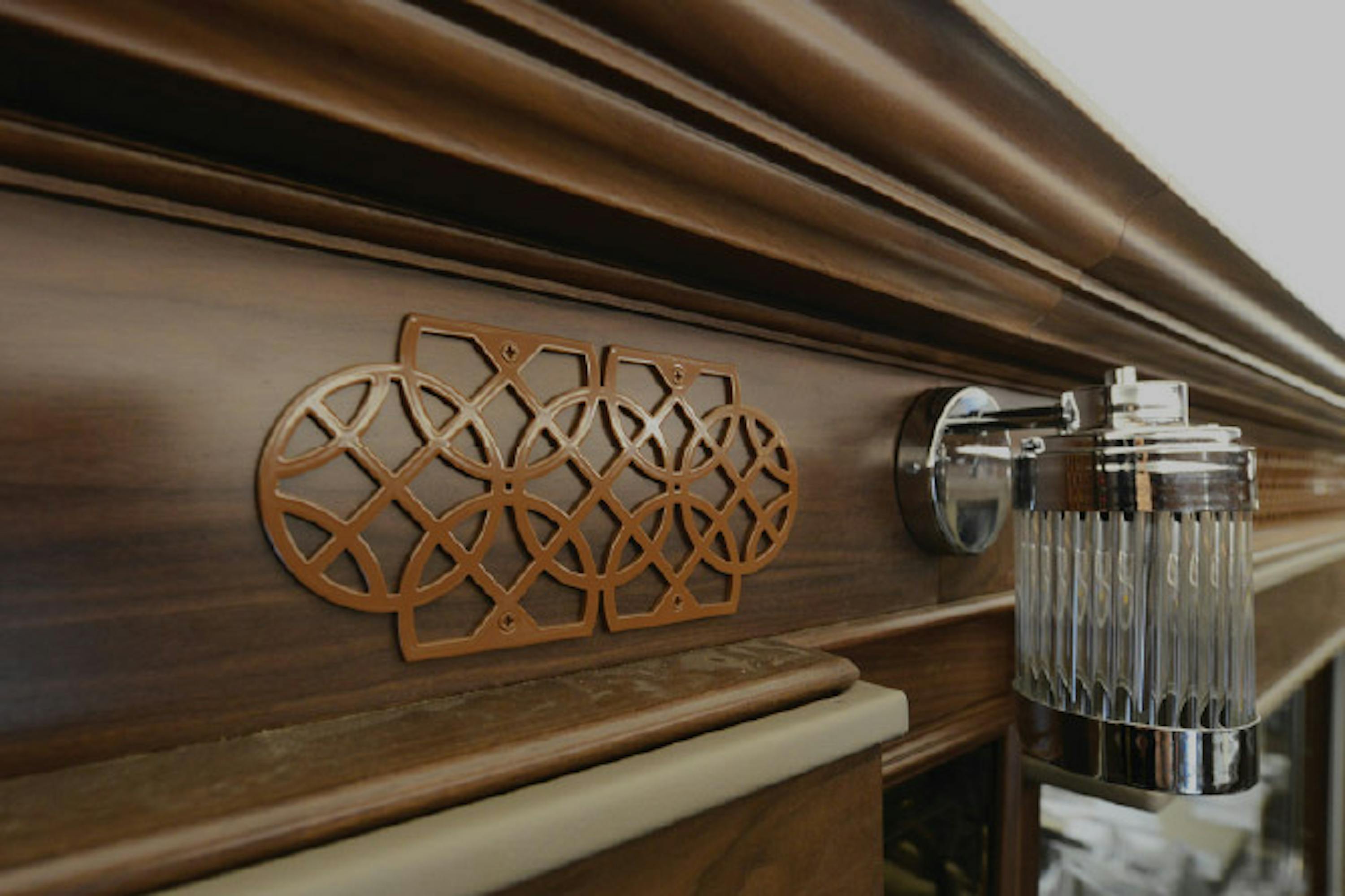 Top of a head board with detailed design attached to wood. Small light attached to head board.