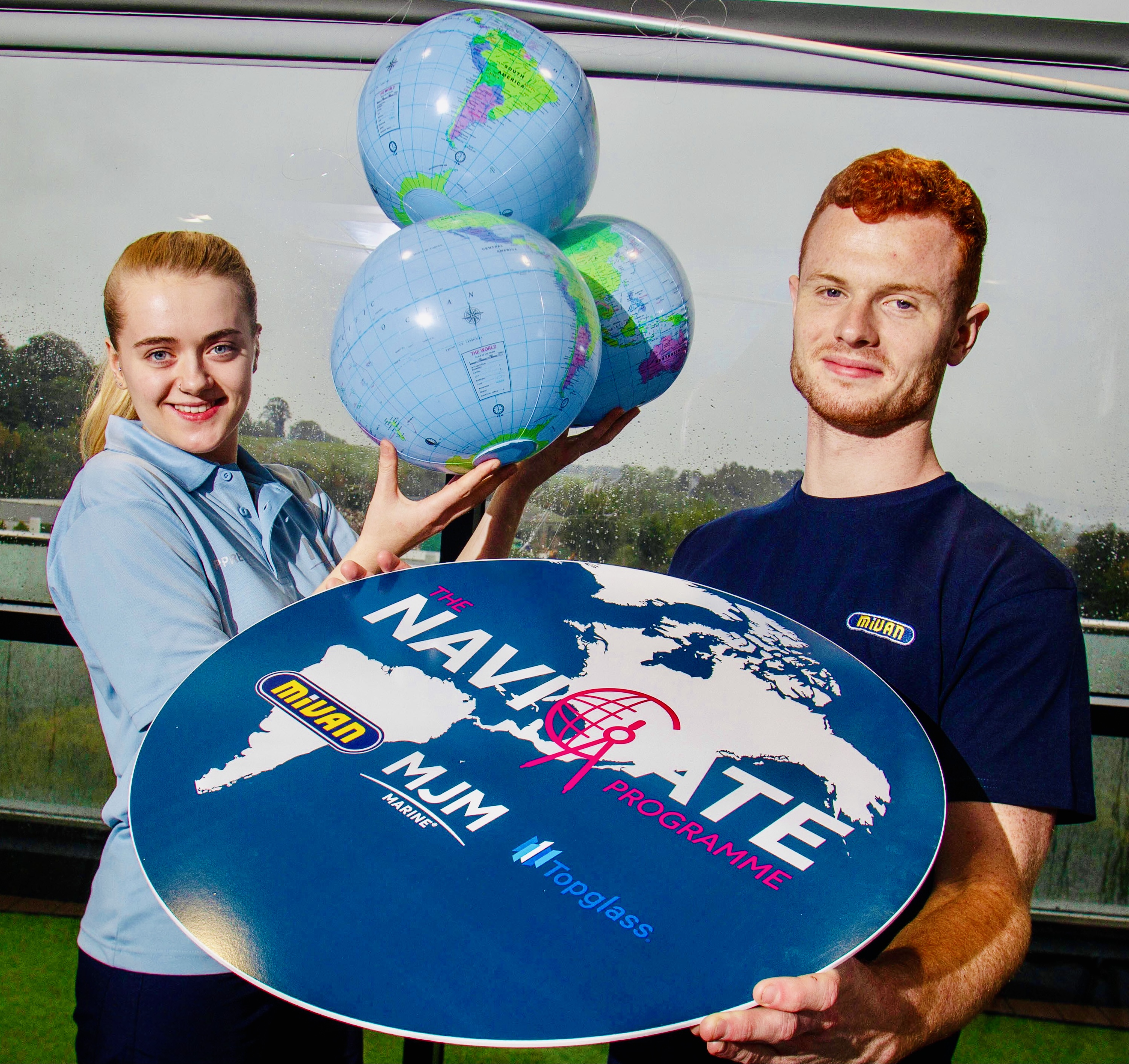 Young lady holding 3 inflatable globes of the world. Young man holding a flat map of the world. Shows the MJM group companies. 