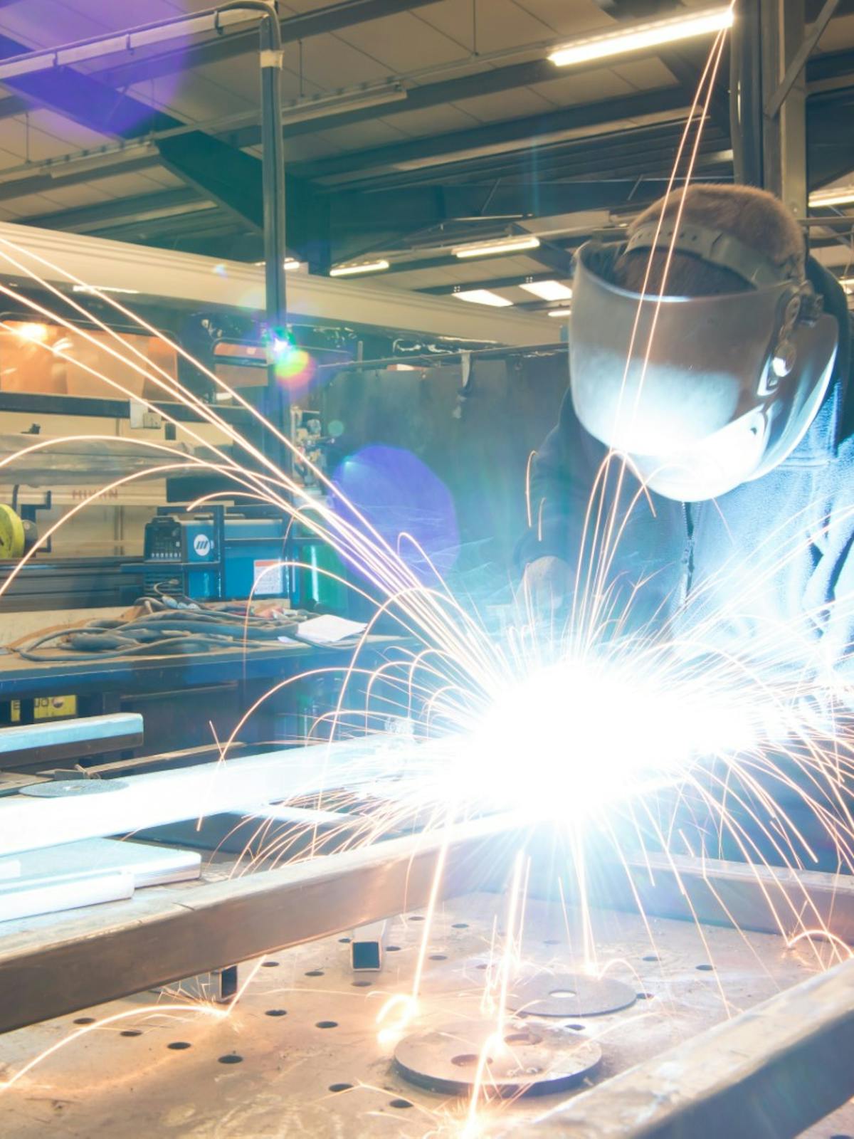 Welder joining two pieces of metal. Sparks fly from the welding. 