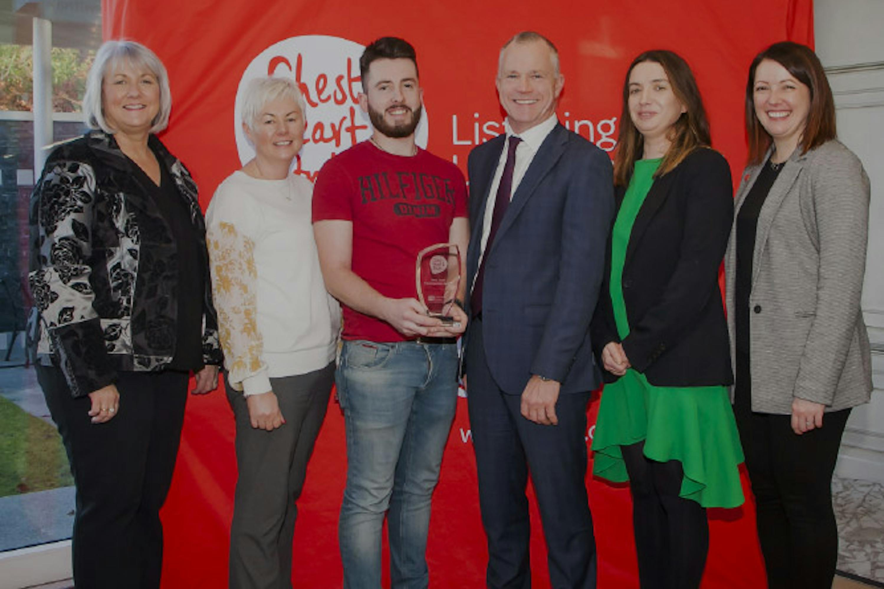 One person accepting a trophy from CEO of Northern Ireland Chest Heart & Stoke with six individuals in picture.  