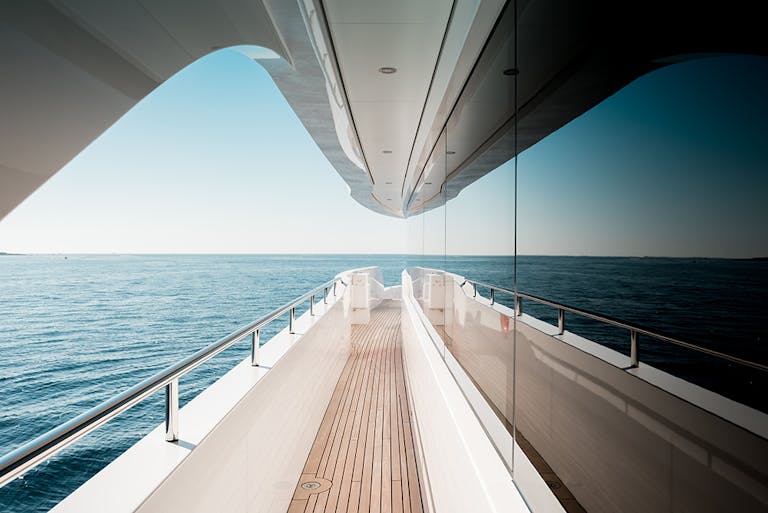 View down the gangway of superyacht with safety railing to the left and reflective window to the right. 