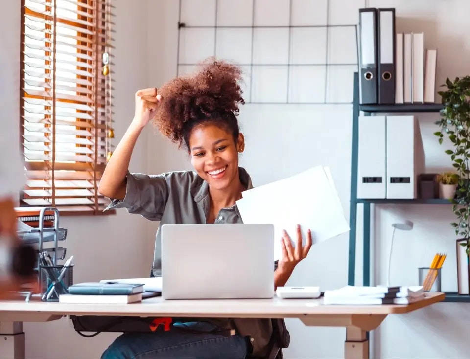 Woman sitting behind a laptop with papers in her left hand