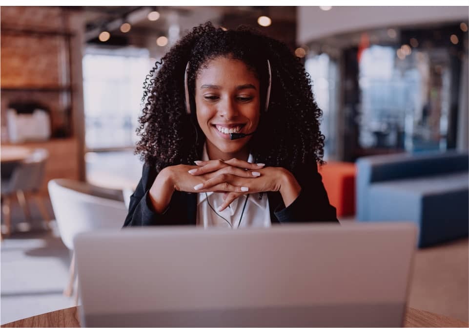 Woman sitting behind a laptop with her hands underneath her face and wearing headphones