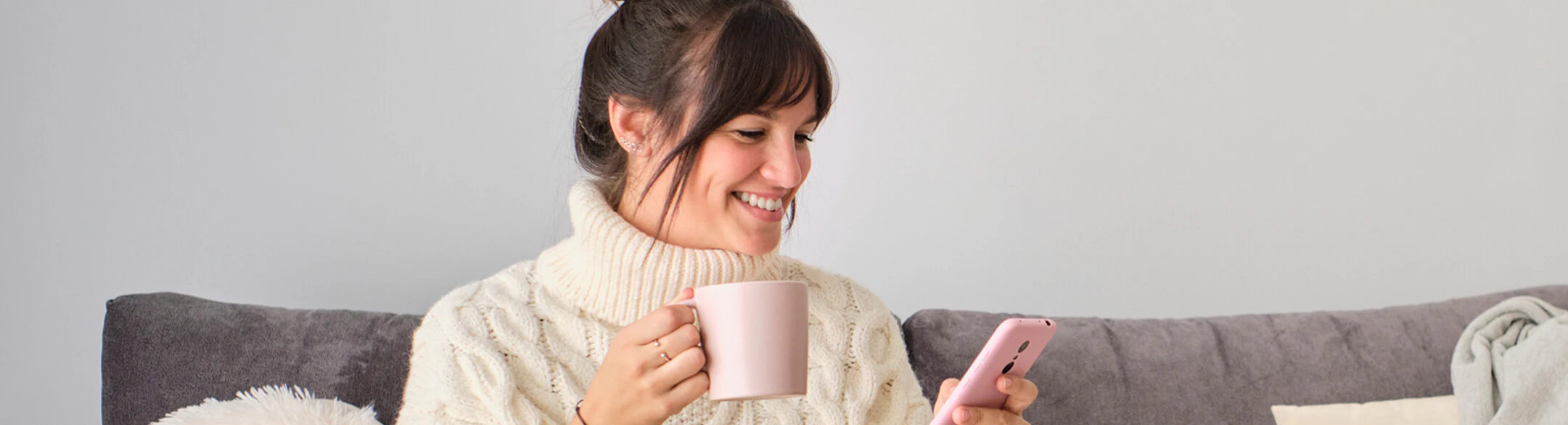 woman on couch drinking coffee loking at phone