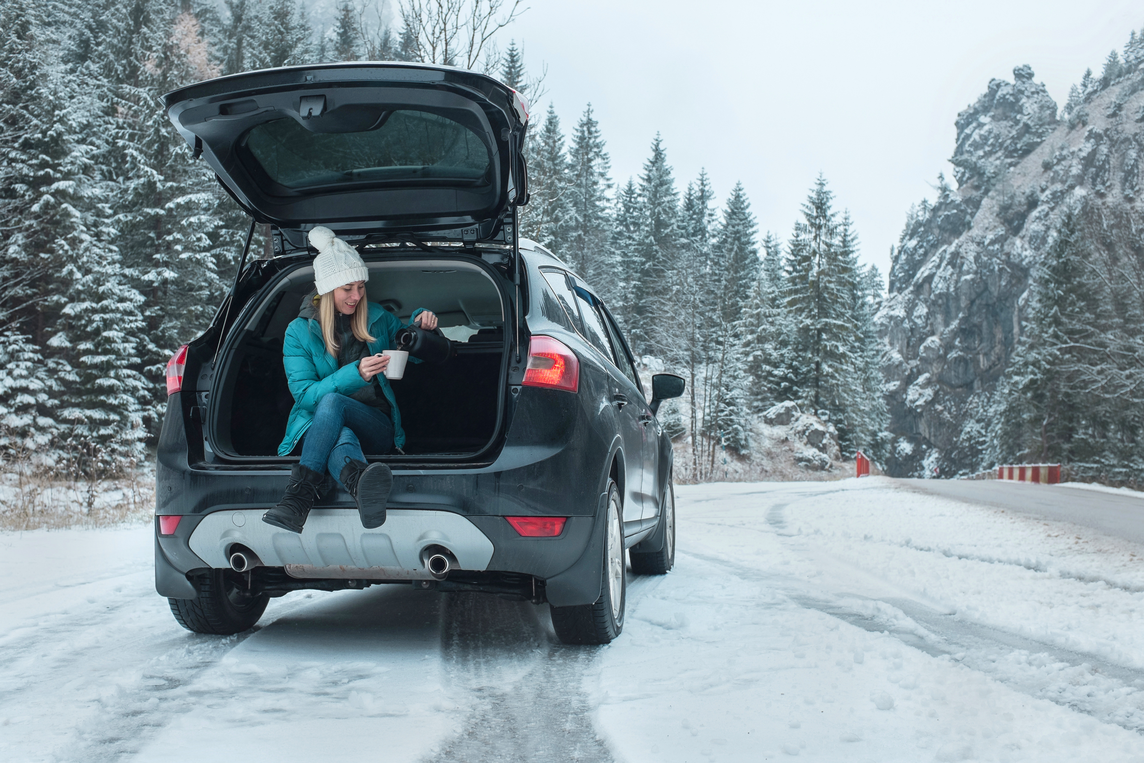 Woman sitting in the boot of a car drinking a coffee