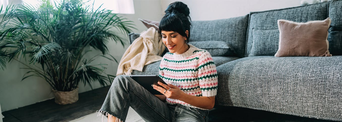 Une femme regarde sa tablette assise devant son canapé