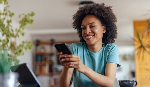 Jeune femme souriant, consultant son téléphone devant son ordinateur