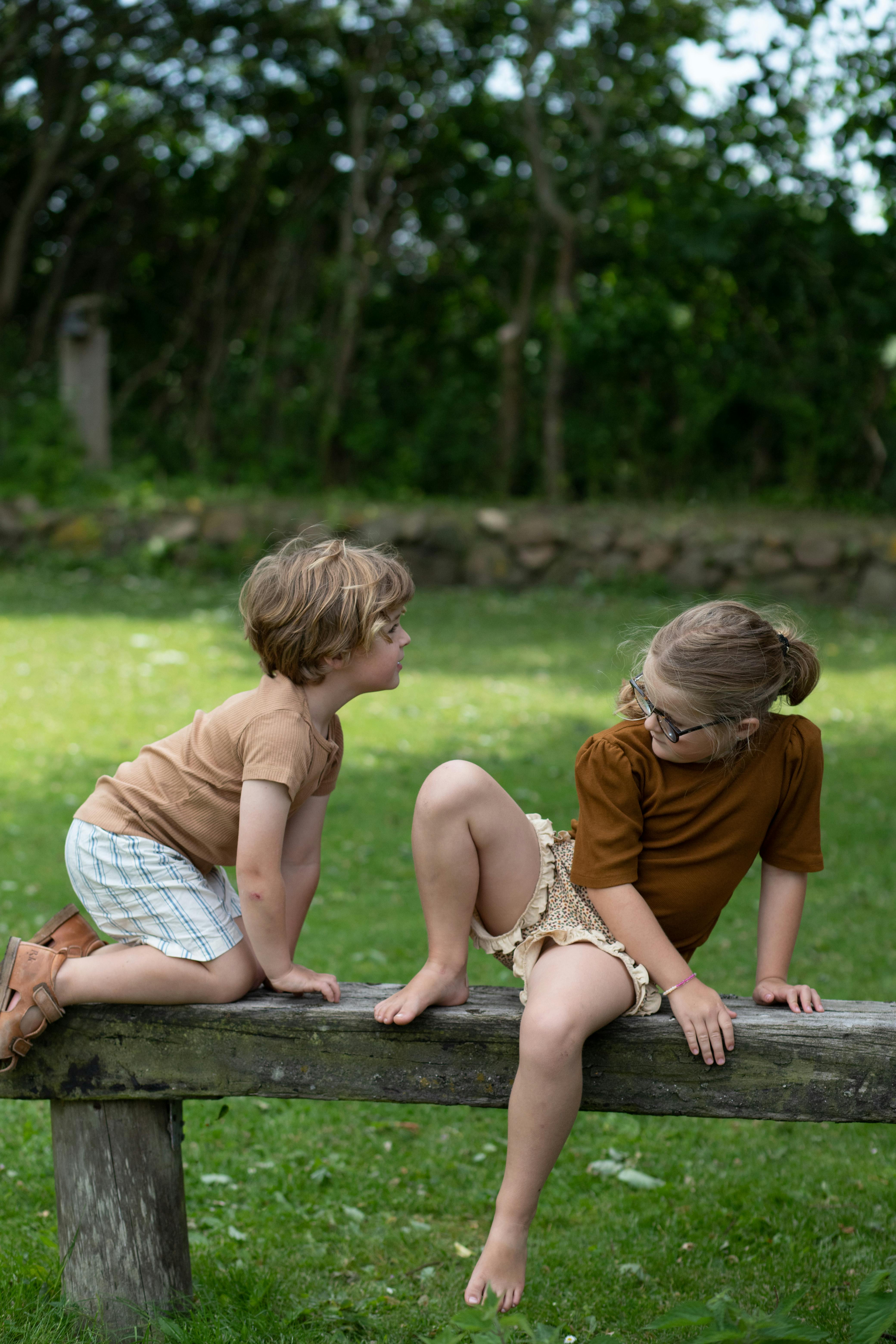 dreng og pige sidder på bænk i have