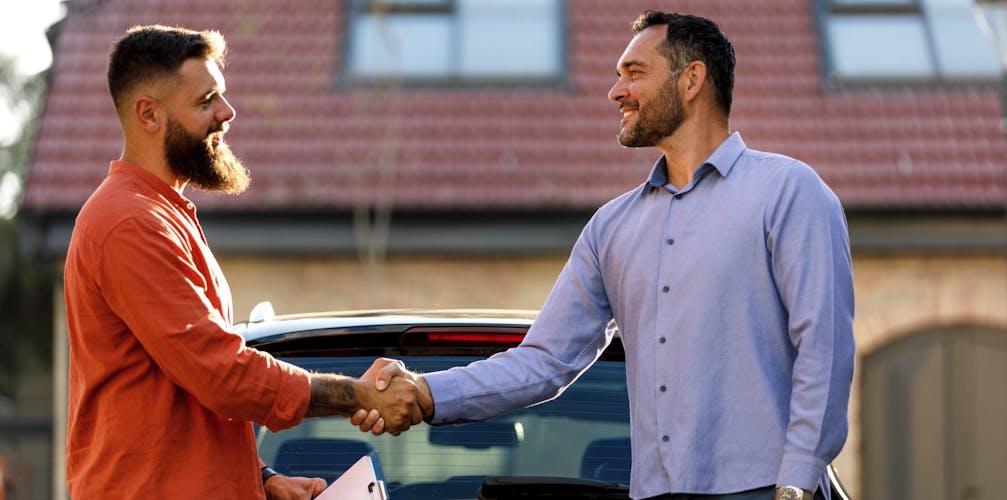 Zwei Männer schütteln Hände vor einem Auto