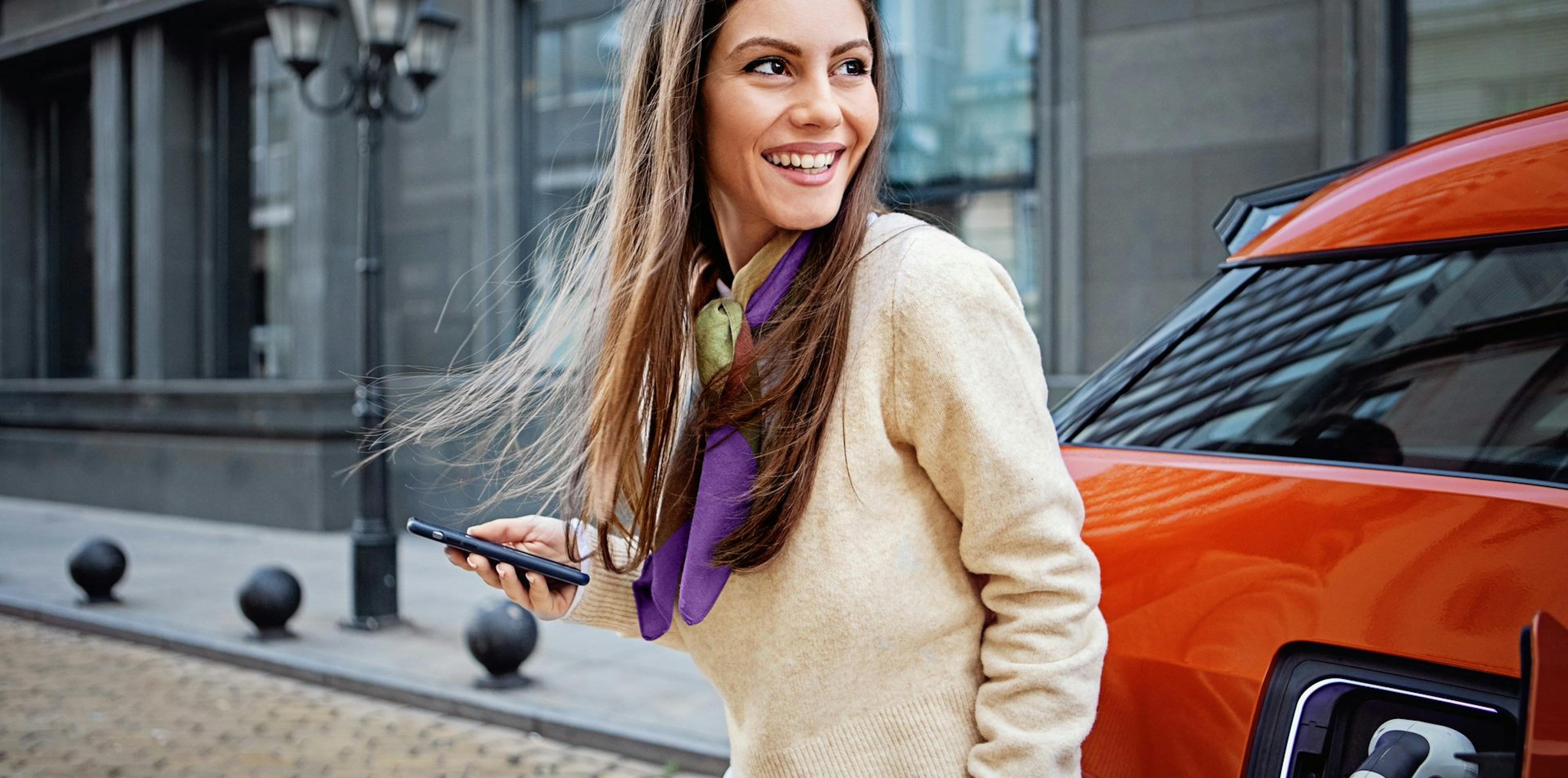 Frau steht mit Handy in der Hand vor einem Auto