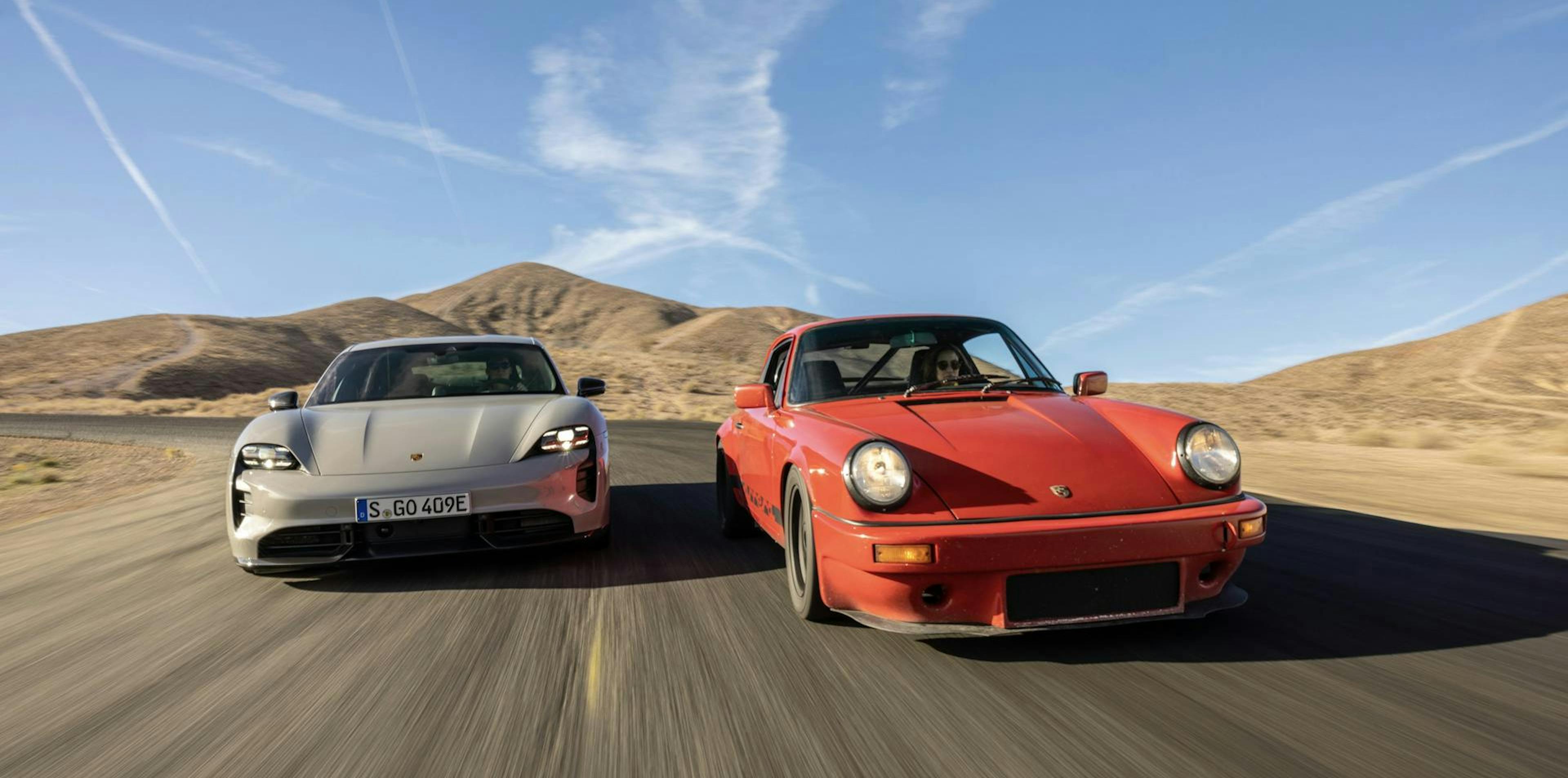 Zwei E-Autos fahren nebeneinander auf einer Straße in einer Wüstenlandschaft