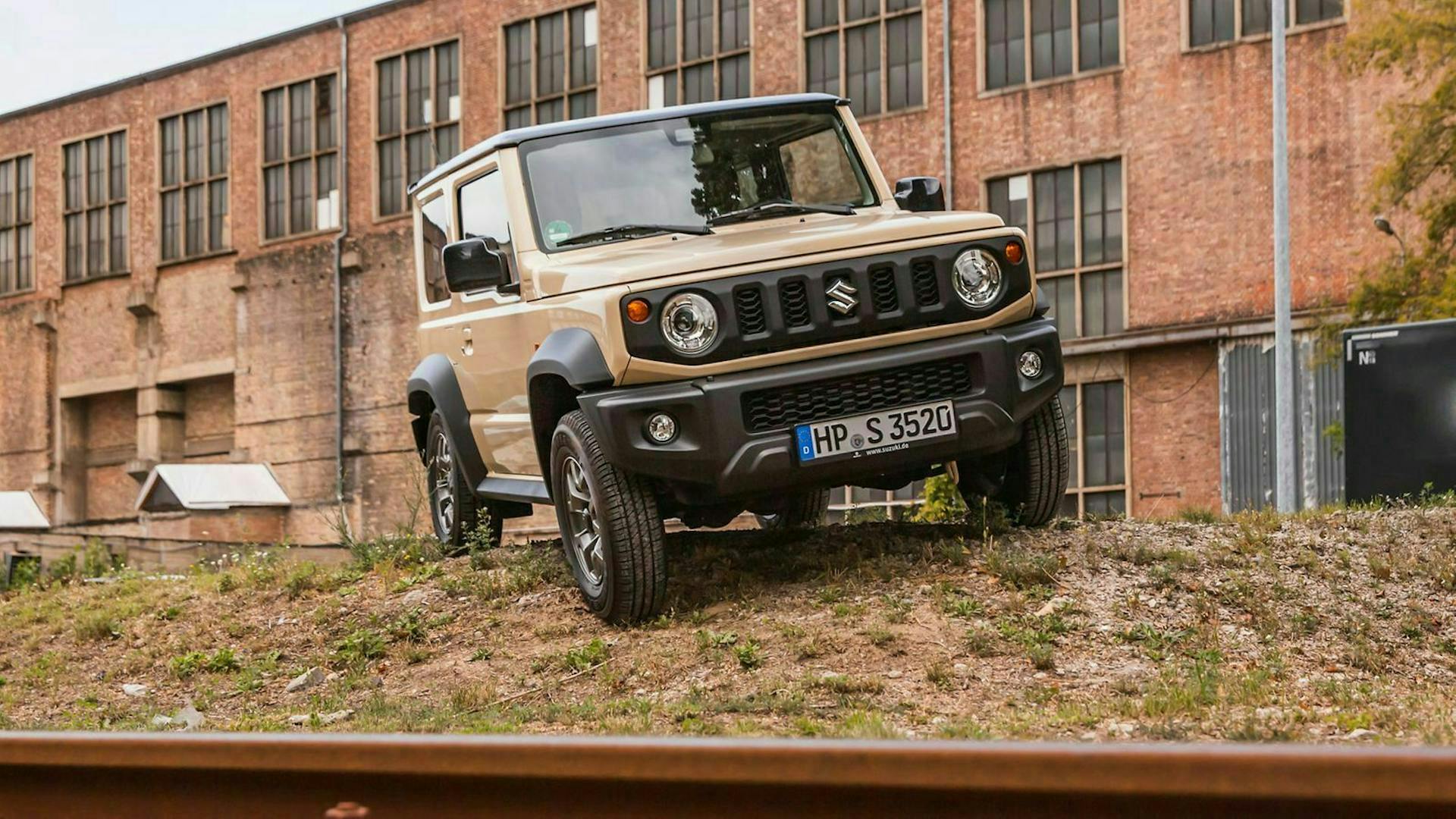 Suzuki Jimny in hellem Orange vor einer Fabrikhalle