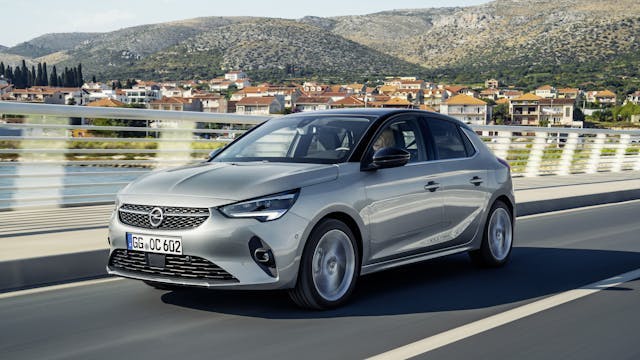 Opel Corsa in Silber fährt über eine Brücke, Häuser im Hintergrund