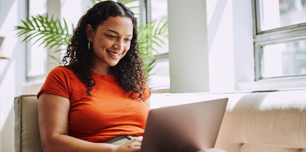 Frau sitzt auf der Couch mit einem Laptop auf dem Schoß