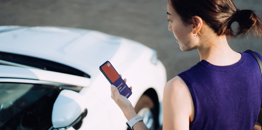 Frau steht am Fahrzeug mit Smartphone an der Hand