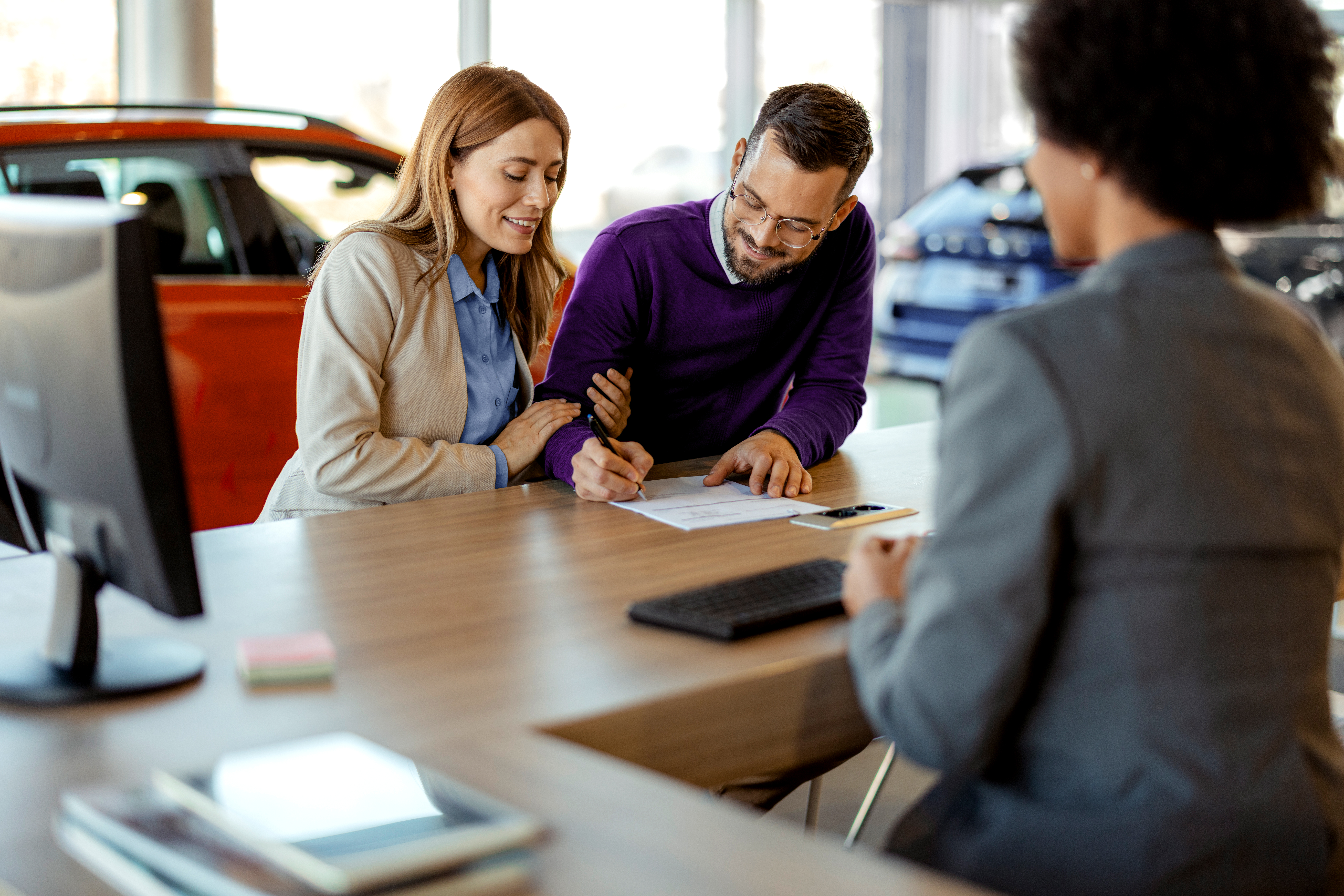 Eine Frau und ein Mann unterschreiben in einem Autohaus einen Vertrag.