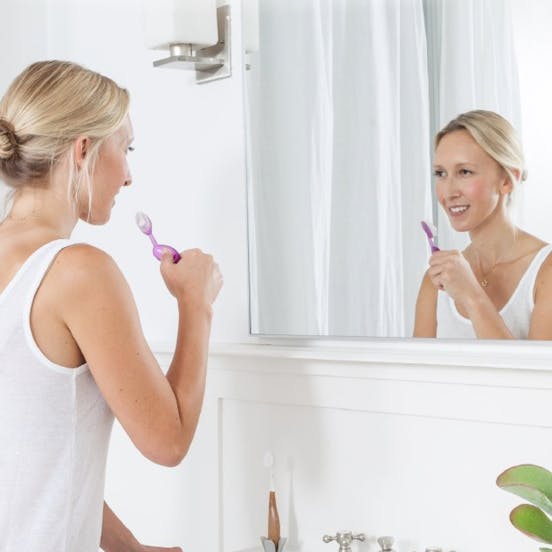 A woman looking at herself on a mirror and about to brush her teeth