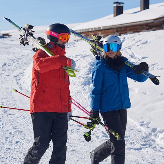 Man and Woman in ski gear walking with skis on their shoulder