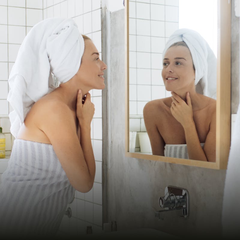 A woman with a towel on her head looking at herself in the mirror