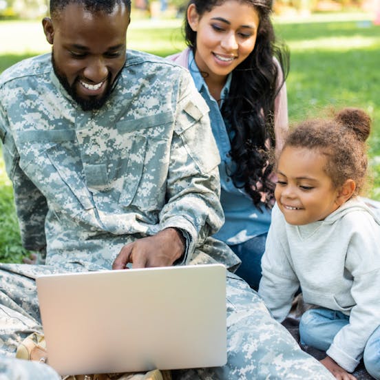 A man wearing military uniform, a woman and a child looking at a computer screen and smiling