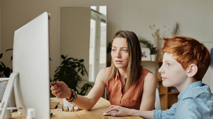 a woman showing something on the computer to a kid