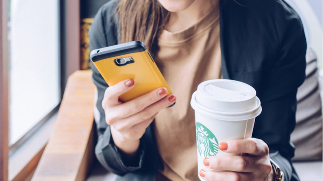 A young woman holding a cellphone and a Starbucks cup