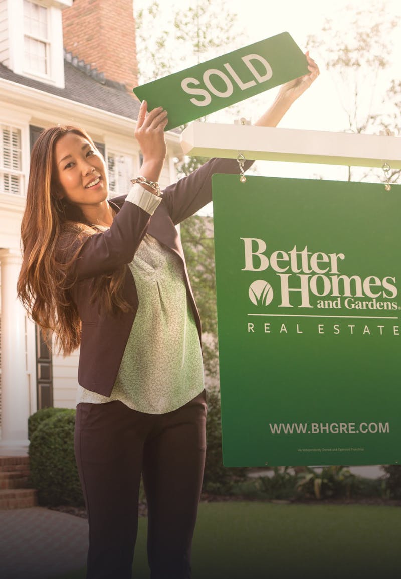 A saleswoman holding a sold sign over a Better Homes and Gardens banner