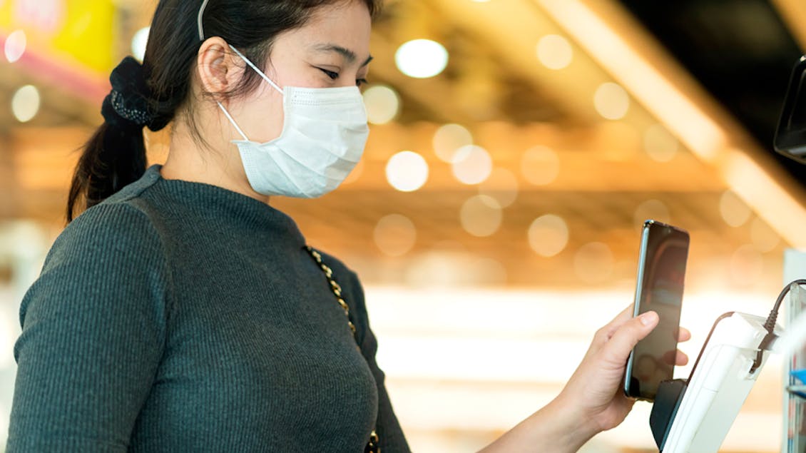 A woman with a mask using her phone to pay 