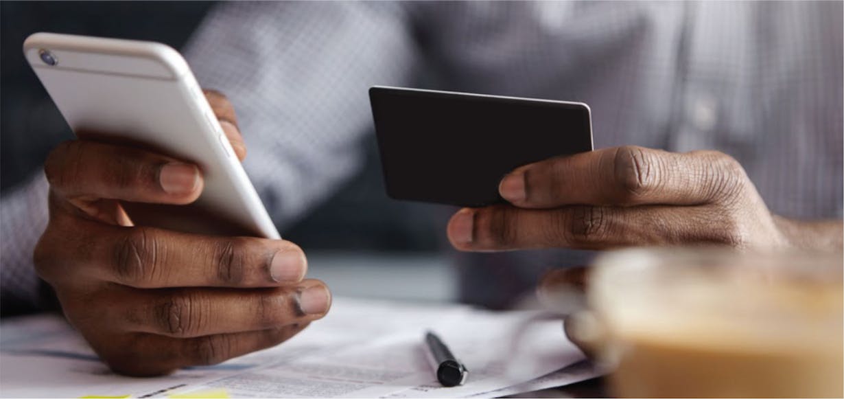 a person looking a phone with a credit card on one hand 