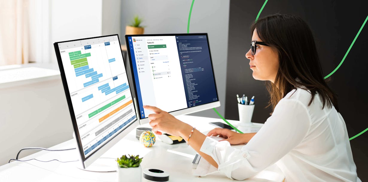 Woman at corporate desk pointing at a schedule with additional monitor to the right