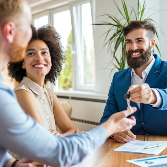 real state seller delivering a key to a man and a woman